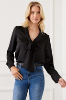 Woman wearing a black blouse with a bow tie and blue jeans against a white background