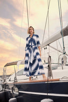 Woman in a blue and white dress standing on a sailboat with a sunset sky.