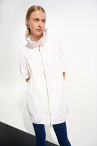 Woman wearing a white jacket with a hood on a plain background