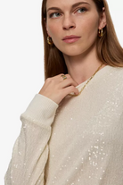 Woman wearing a beige sequin sweater with a plain background