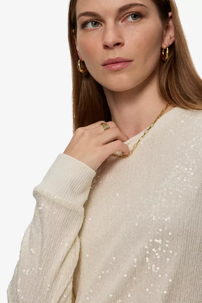 Woman wearing a beige sequin sweater with a plain background