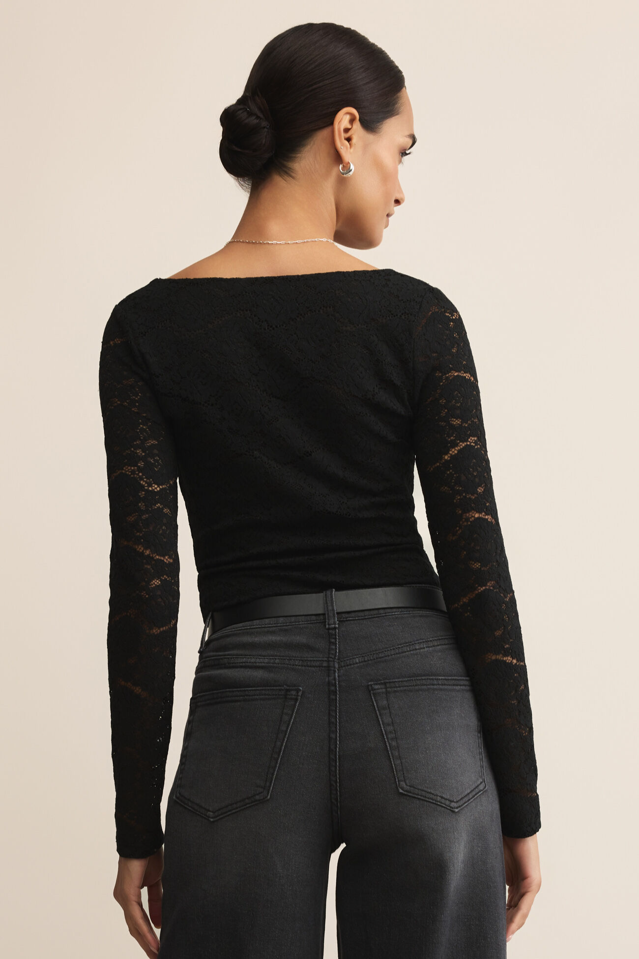 Woman wearing a black long-sleeve top with lace details and black pants on a beige background