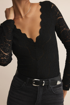 Black lace top worn by a person on a beige background