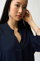 Woman wearing a dark blue top with long earrings and a bracelet on a plain background