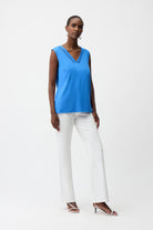 Woman wearing a blue sleeveless top and white pants on a white background