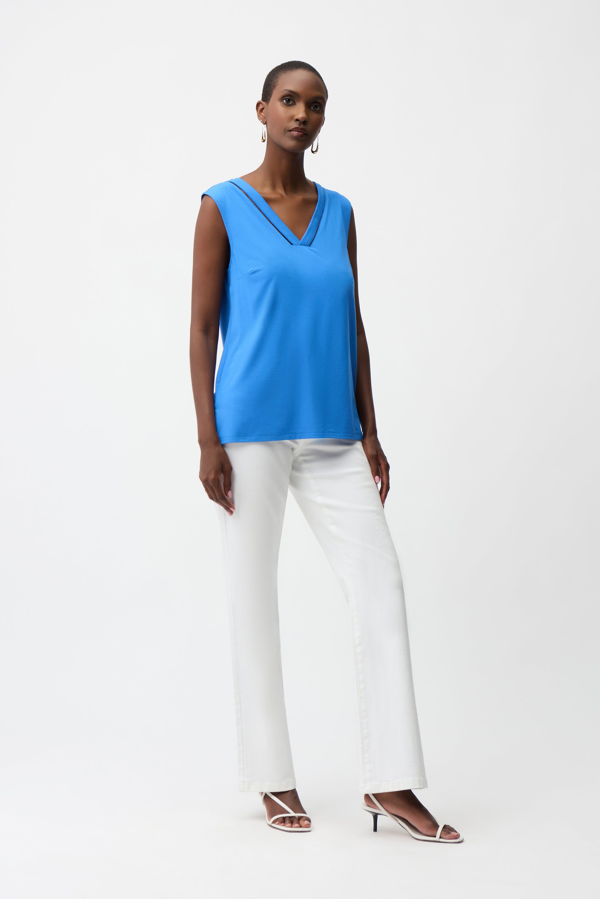 Woman wearing a blue sleeveless top and white pants on a white background