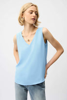 Woman wearing a light blue sleeveless top and jeans on a white background