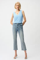 Woman wearing a light blue sleeveless top and jeans on a white background