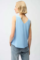 Person wearing a light blue sleeveless top and gray jeans on a white background