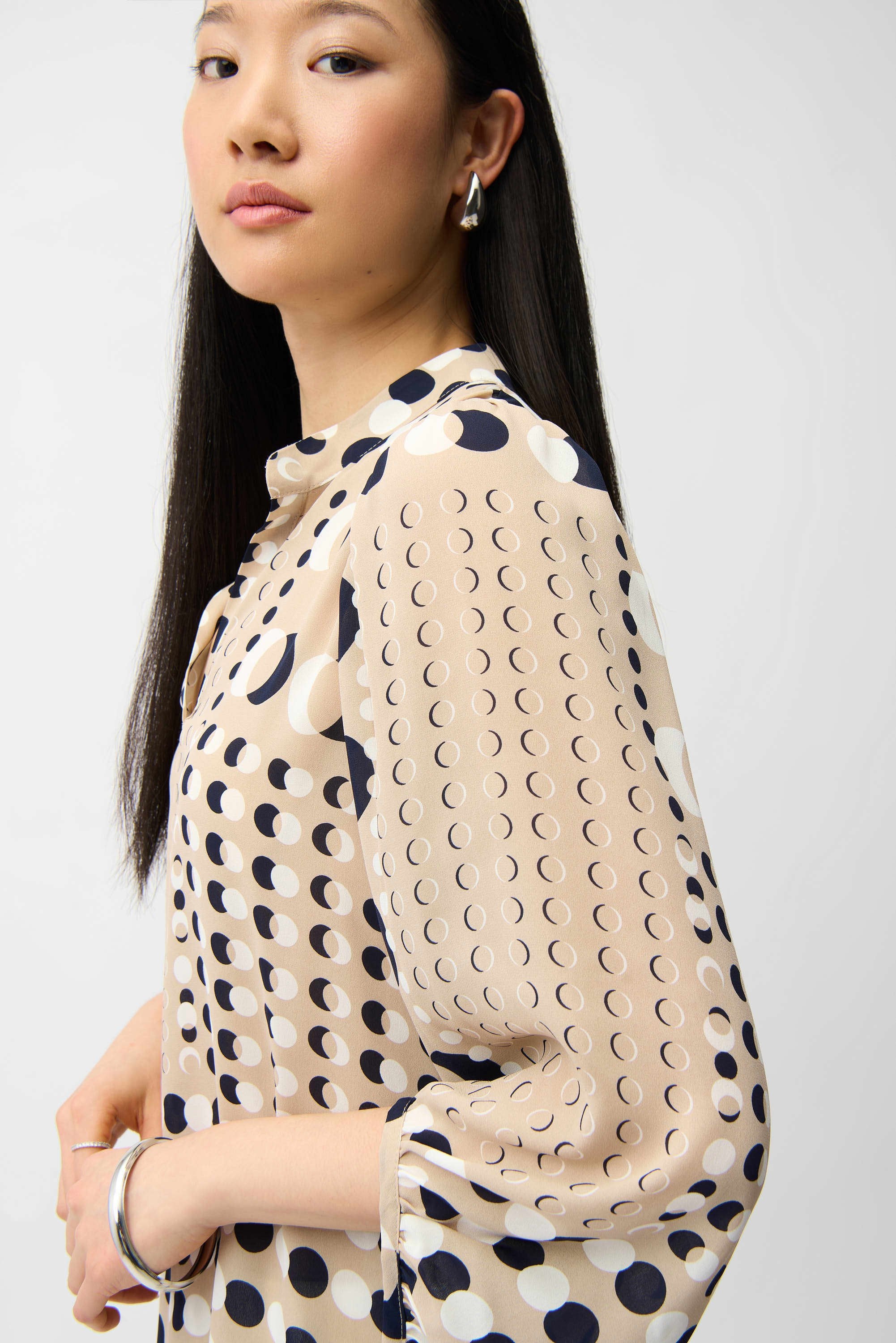 Woman wearing a beige blouse with black polka dot pattern on a white background