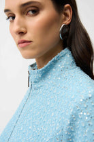 Close-up of a person wearing a light blue sequined jacket with a plain background