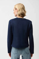 Person wearing a navy long-sleeve top with studded details on a white background