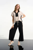 Woman wearing a white blouse with black accents and black pants on a reflective surface.