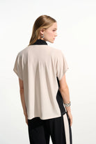 Woman wearing a beige top with black accents on a white background
