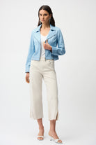 Woman wearing a light blue jacket, white top, and white pants on a white background