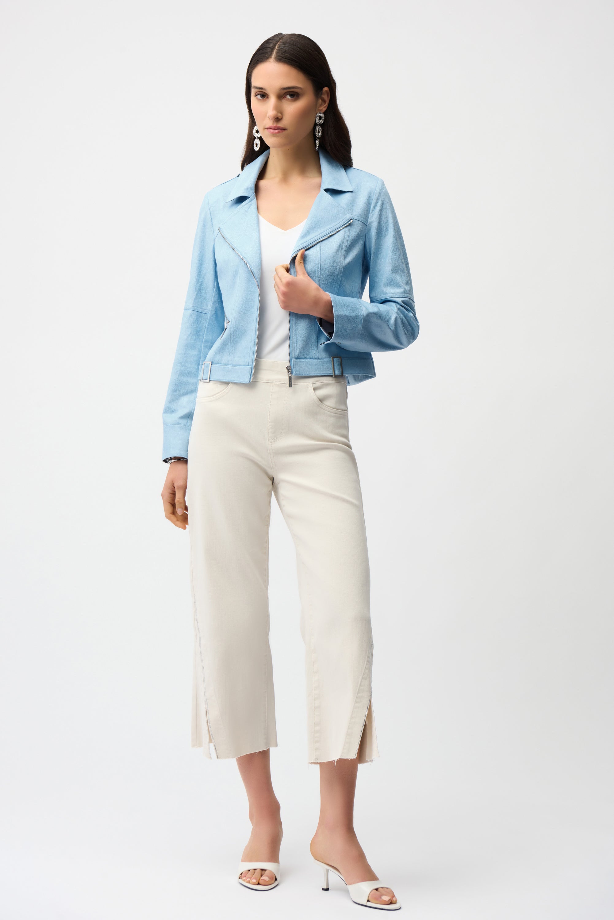 Woman wearing a light blue jacket, white top, and white pants on a white background