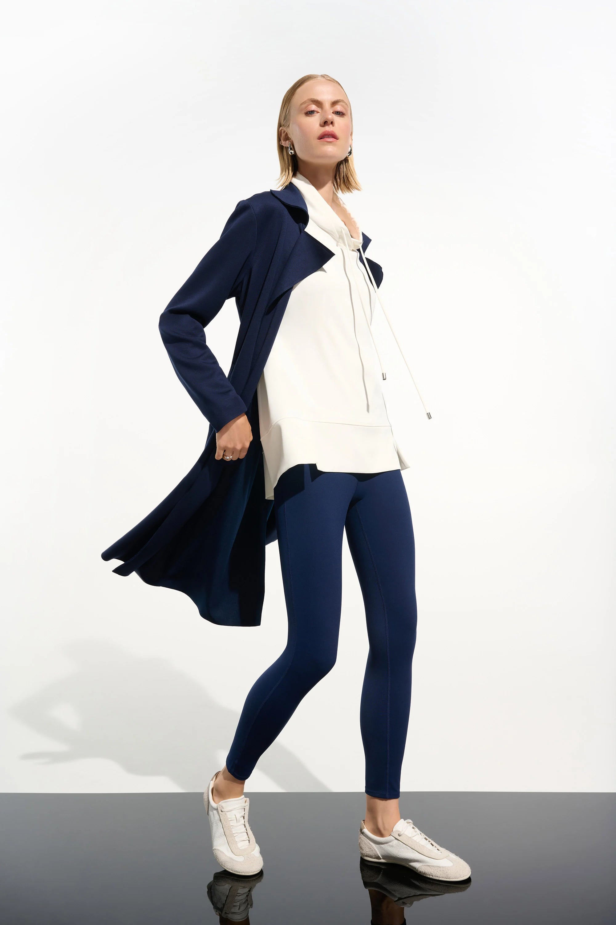 Woman wearing a navy cardigan, white shirt, and blue leggings on a white background