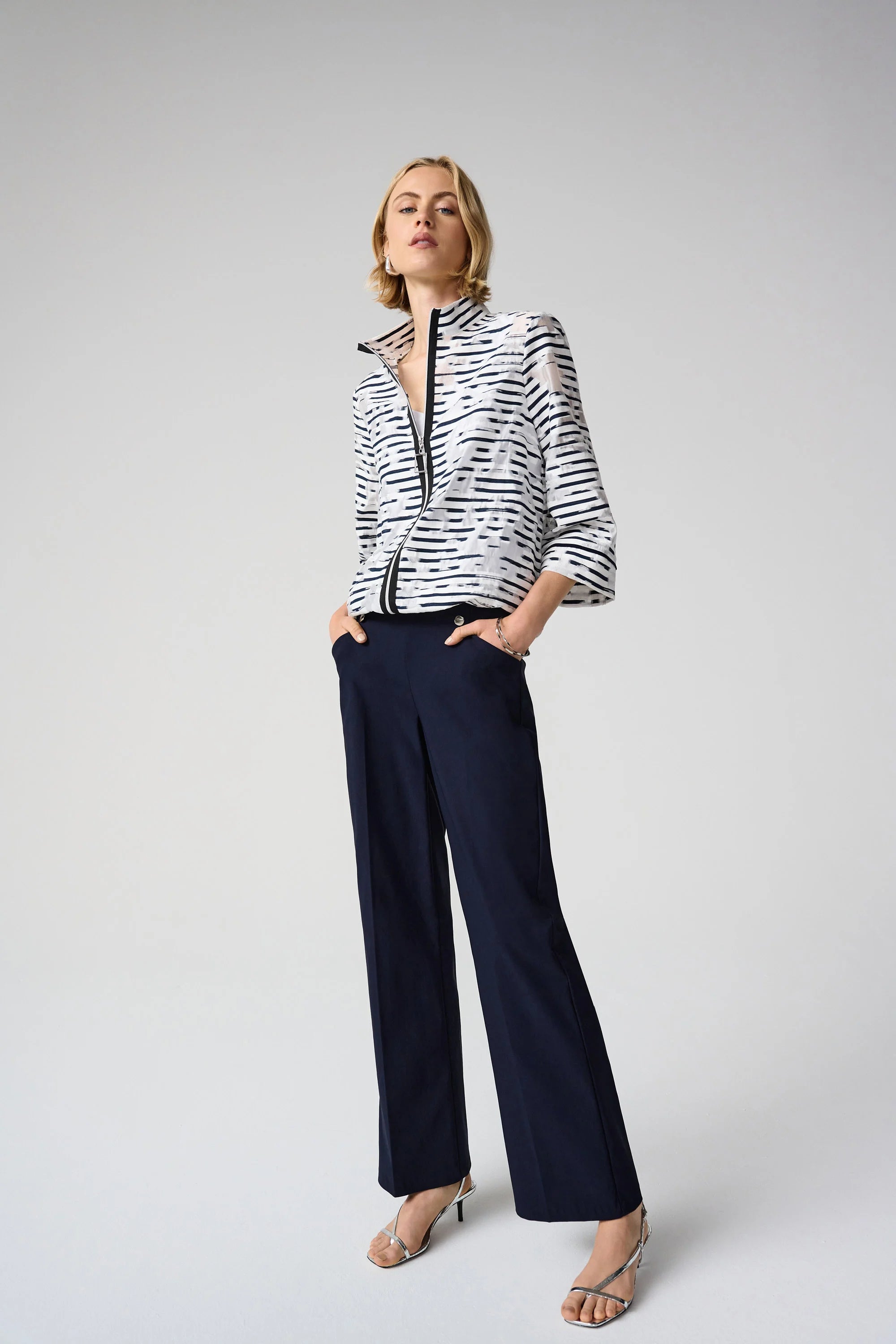Woman wearing a black and white patterned jacket and navy pants on a white background