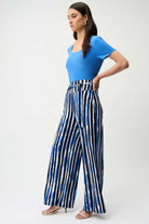 Woman wearing a blue top and black and white striped pants on a white background