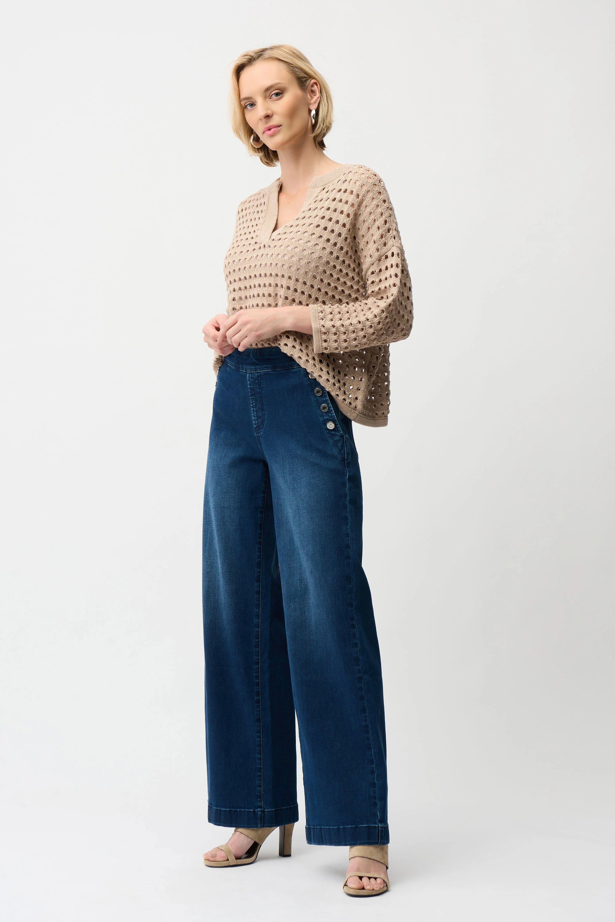 Woman wearing a beige knitted sweater and blue jeans on a white background