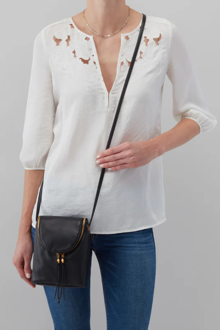 Person wearing a white blouse with bird patterns and blue jeans, holding a black handbag against a gray background