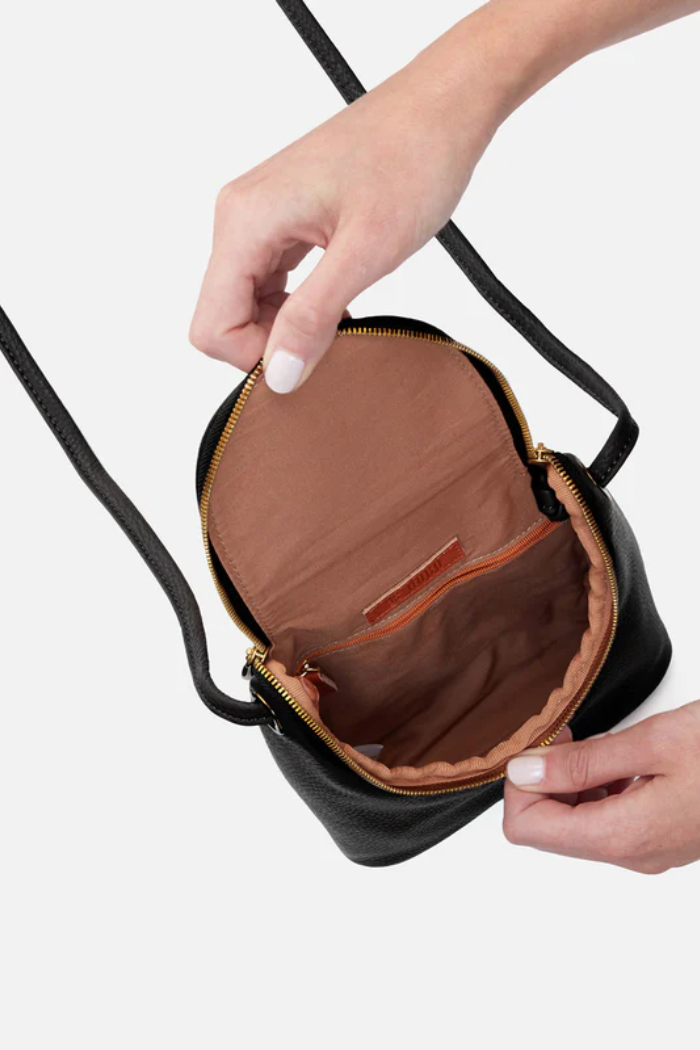 Black handbag with a brown interior, held open by hands on a white background
