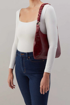 Person wearing a white long-sleeve top, blue jeans, and carrying a red handbag on a plain background