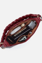 Red leather crossbody bag with braided handle, open to reveal items on a white background