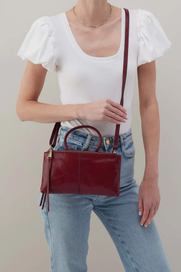 Person wearing a white top and blue jeans holding a red handbag against a plain background