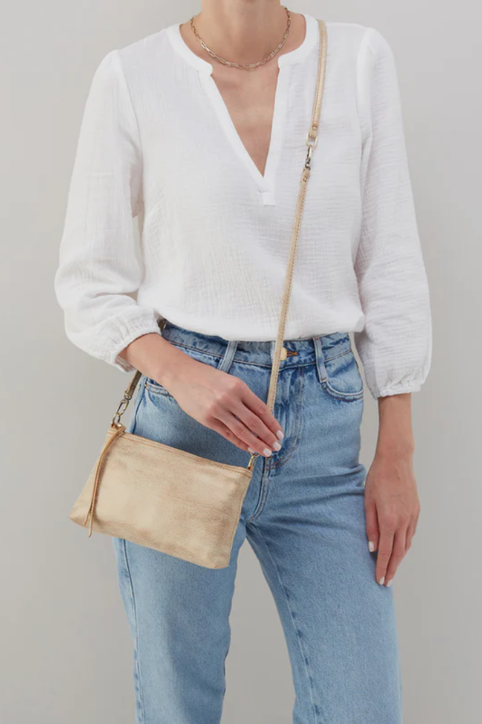 Person wearing a white blouse and blue jeans with a beige handbag on a plain background
