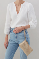 Person wearing a white blouse and blue jeans with a beige handbag on a plain background