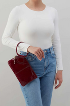 Person wearing a white long-sleeve top and blue jeans, holding a red handbag against a plain background