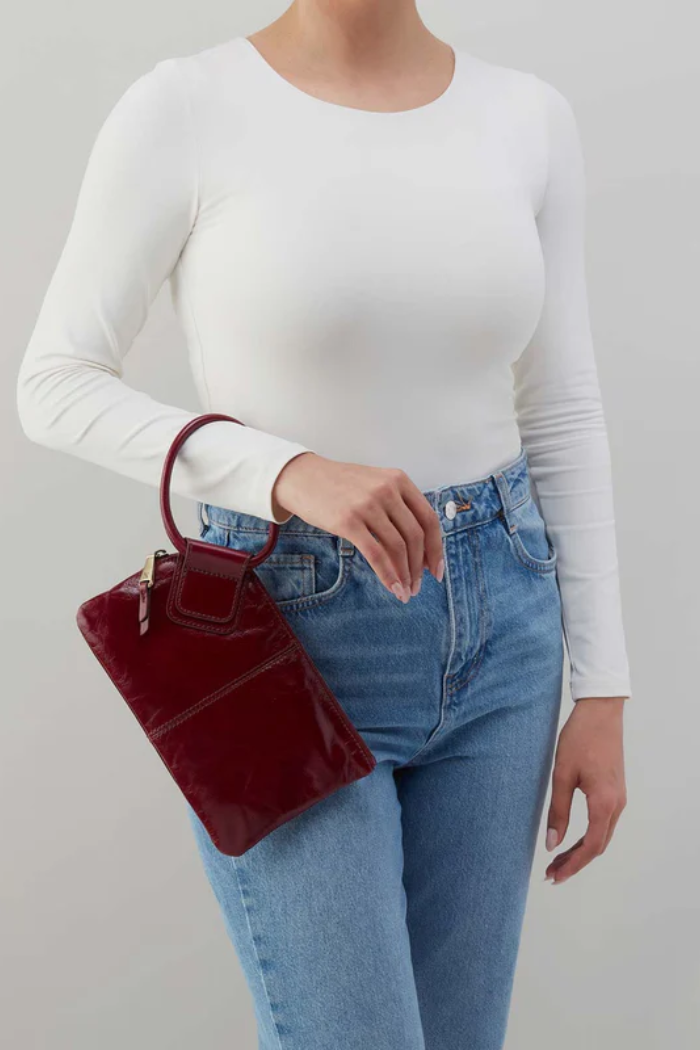 Person wearing a white long-sleeve top and blue jeans, holding a red handbag against a plain background