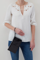 Person wearing a white blouse with floral embroidery and blue jeans, holding a black clutch.