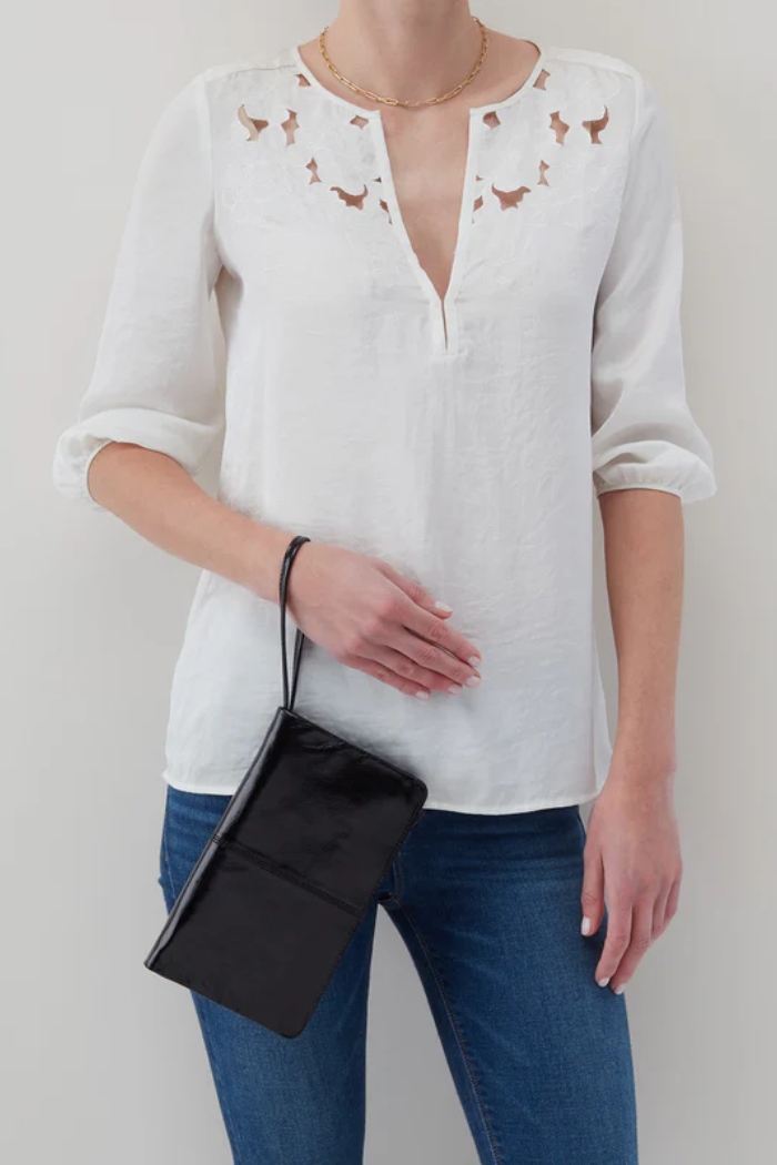Person wearing a white blouse with floral embroidery and blue jeans, holding a black clutch.