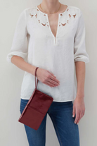Person wearing a white blouse with embroidery and blue jeans, holding a red handbag against a plain background