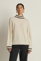 Woman wearing a cream sweater with black and navy trim on a beige background