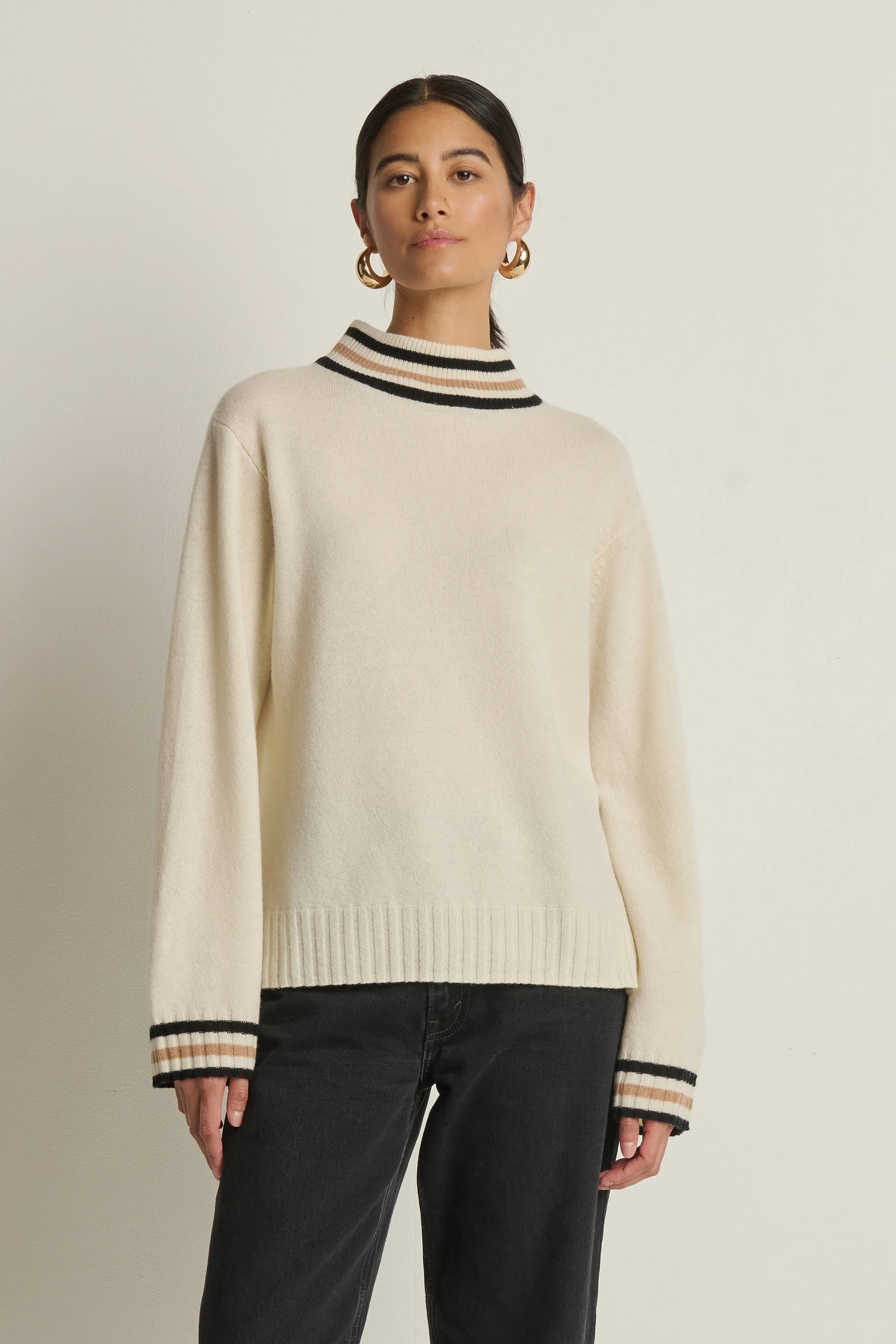 Woman wearing a cream sweater with black and navy trim on a beige background
