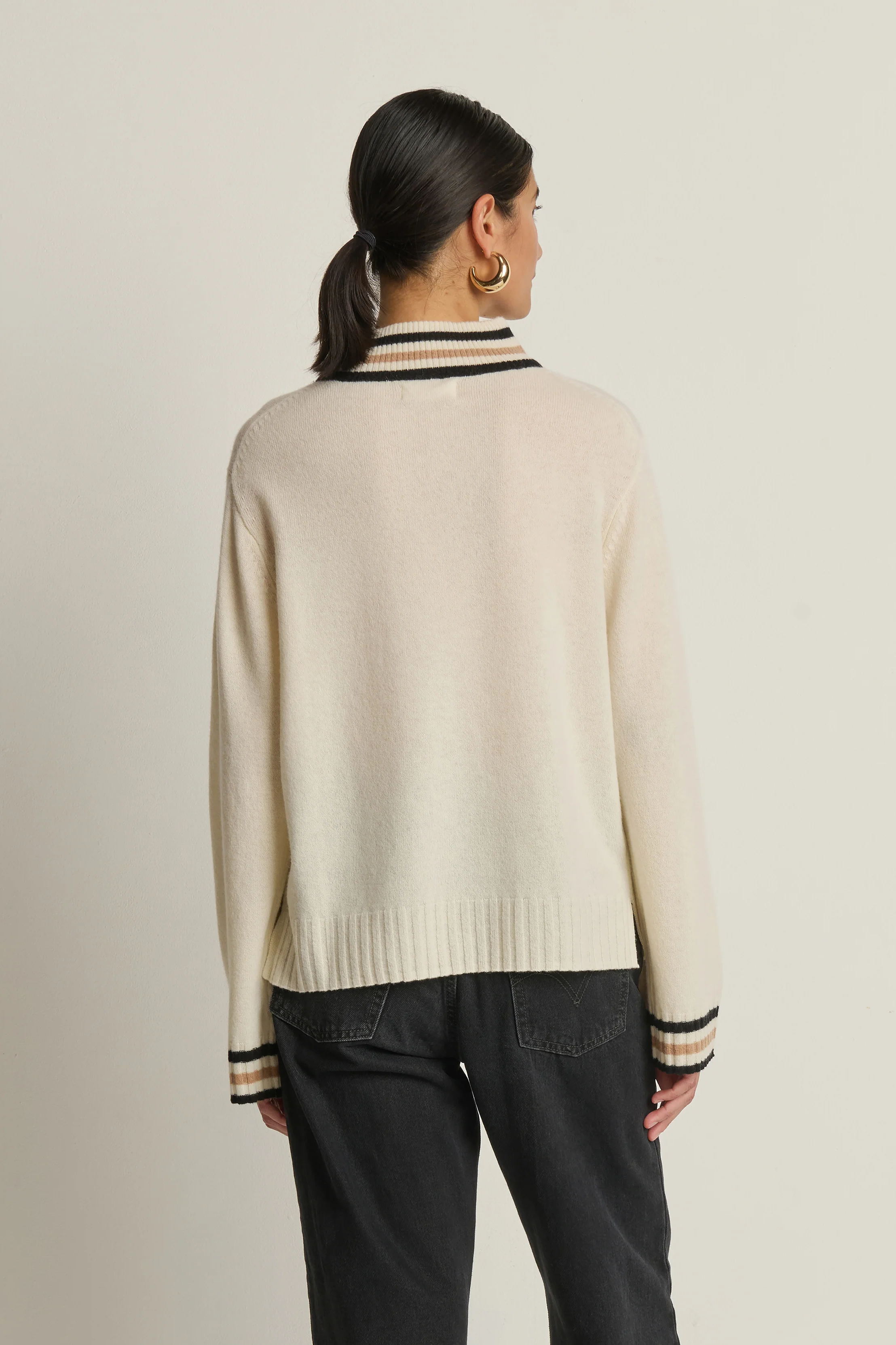 Person wearing a beige sweater with black and white trim on a plain background