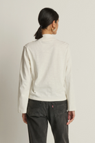 Person wearing a white jacket and dark jeans on a plain background