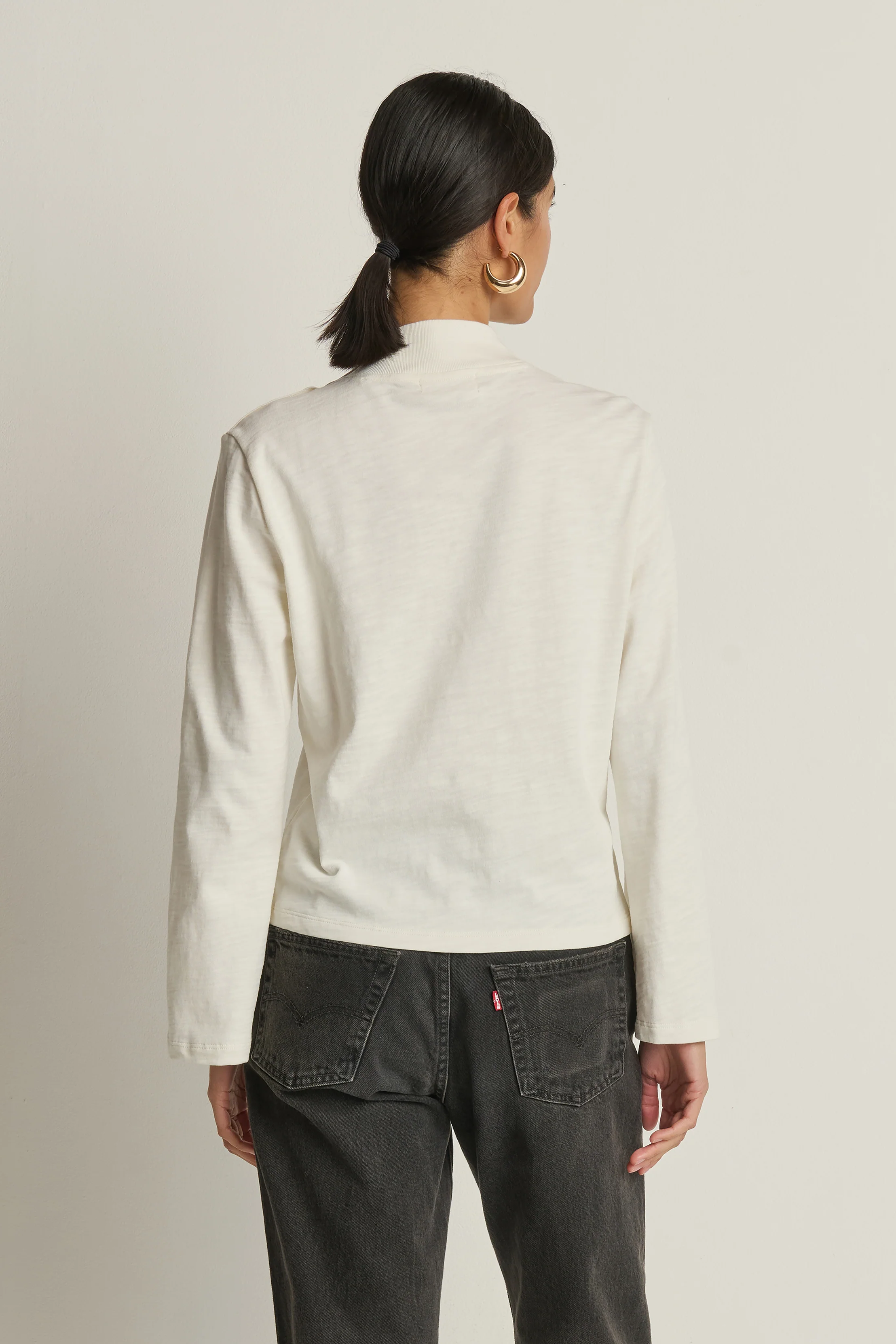 Person wearing a white jacket and dark jeans on a plain background
