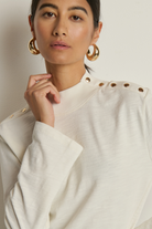 Woman wearing a white top with gold buttons against a neutral background