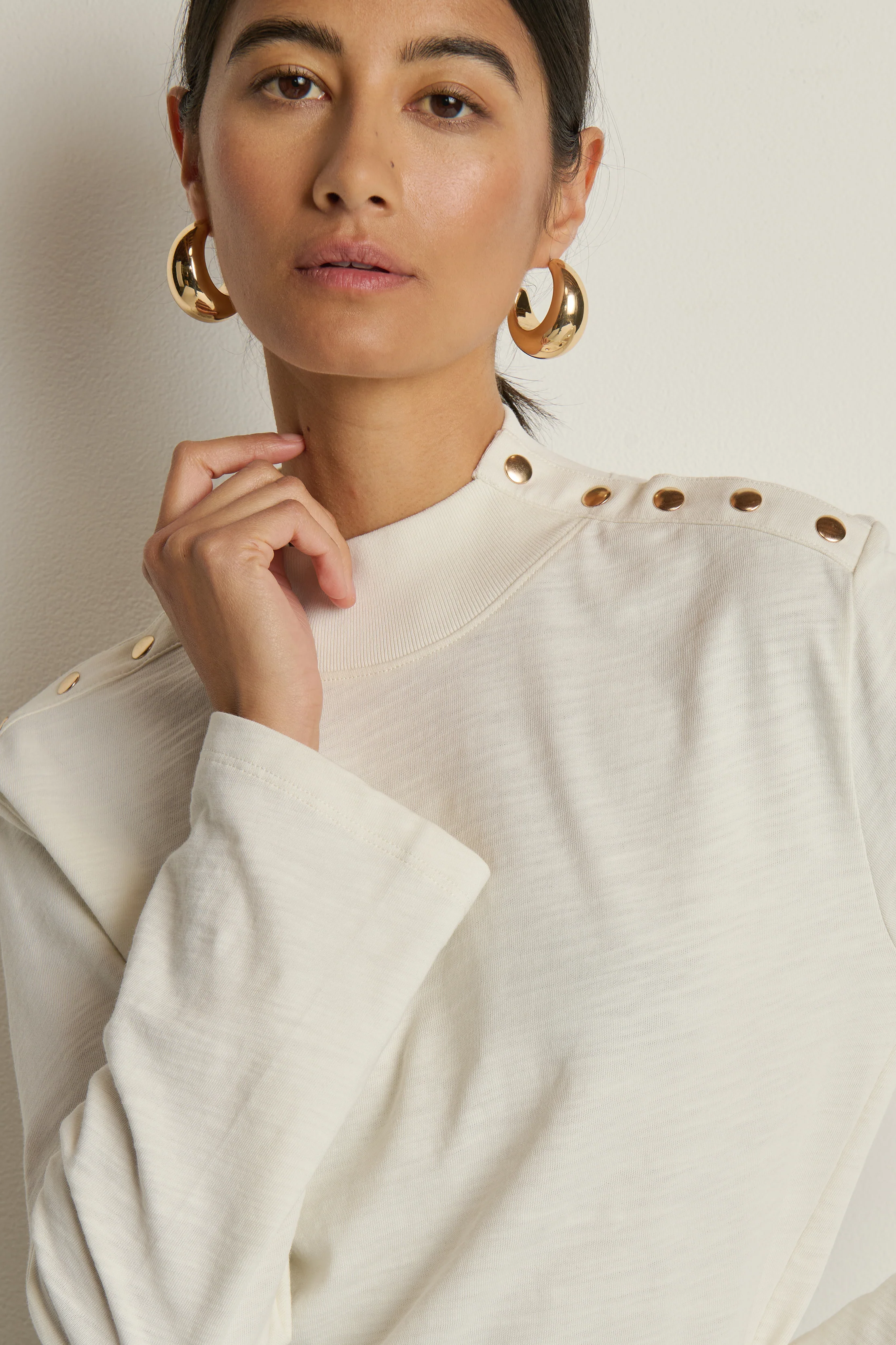 Woman wearing a white top with gold buttons against a neutral background