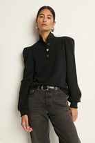 Person wearing a black blouse with puffed sleeves and high-waisted jeans against a plain background