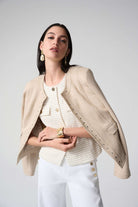 Woman wearing a beige blazer over a white top and pants on a plain background