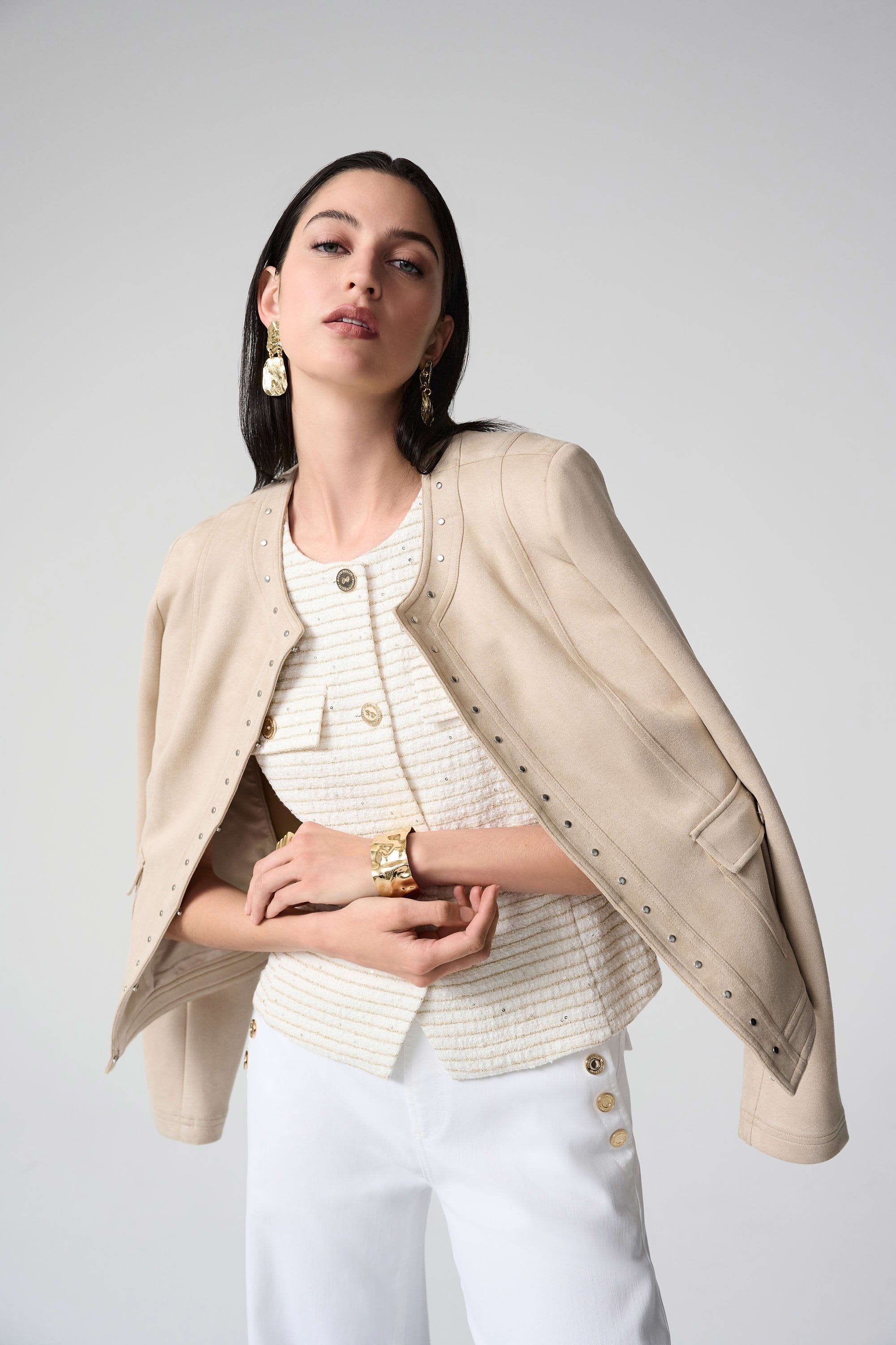 Woman wearing a beige blazer over a white top and pants on a plain background