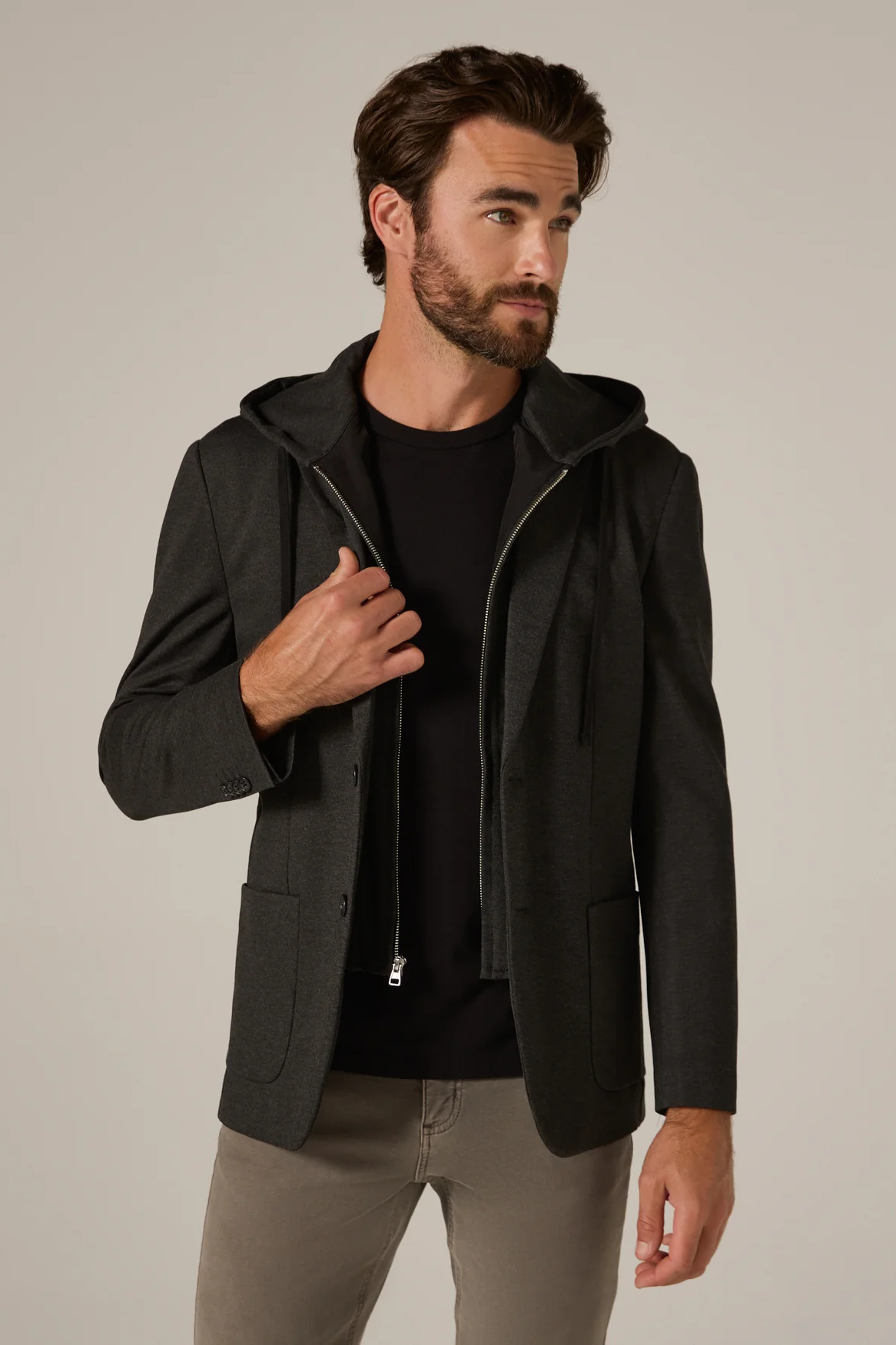 Man wearing a black hooded jacket over a black shirt on a beige background