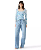 Woman wearing a blue floral top and jeans on a white background