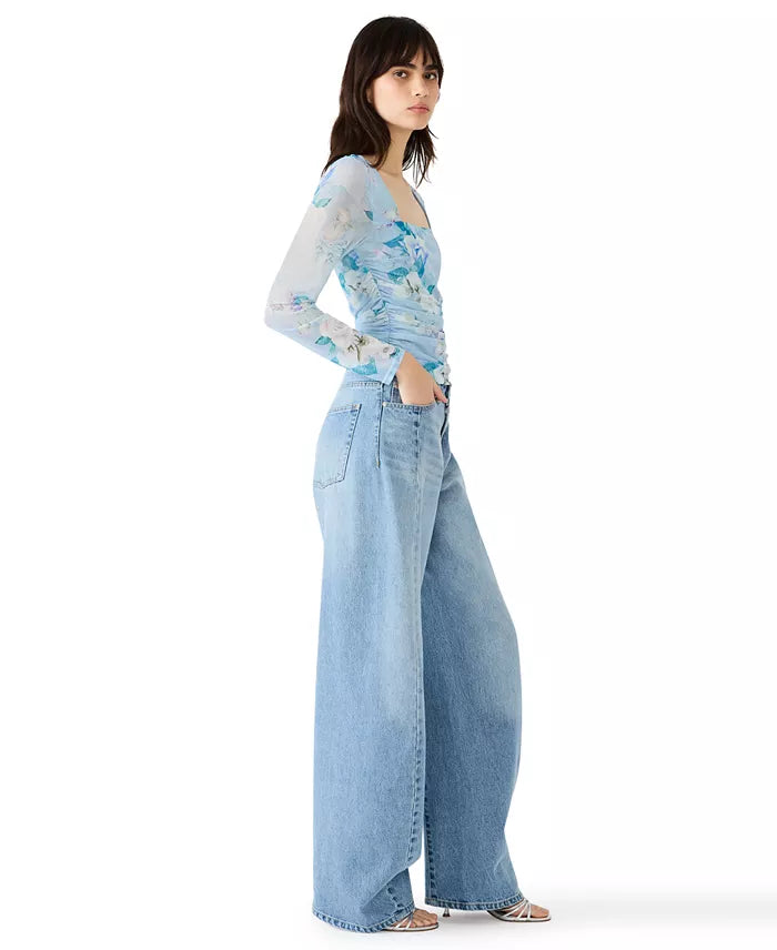 Woman wearing a light blue floral top and wide-leg jeans on a white background