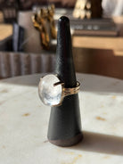 Ring with a white stone on a black stand on a marble surface